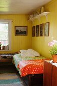 Einzelbett mit bunten Tagesdecken in gelb lackierter Zimmerecke in rustikalem Raum