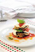 A stack of fried aubergine slices, tomatoes and mozzarella with tomato sauce and basil
