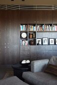 Dunkler Wohnzimmerschrank mit Büchern und Bildern; graues Sofa im Vordergrund