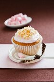 A cupcake decorated with coconut cream and served with mini marshmallows