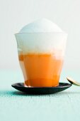 An orange and carrot smoothie topped with warm coconut foam