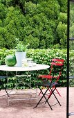 Blick durch offene Terrassentür auf farbige Klappstühle und Gartentisch vor berankter Efeu Mauer und Waldrand