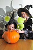 Two girls in Halloween costumes preparing a pumpkin for carving