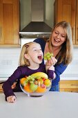 A mother feeding her daughter grapes in the kitchen