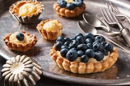 Silver cutlery and various different sized blueberry tarts with lemon cream, one with a bite taken out