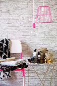 Verchromter Beistelltisch mit Badutensilien neben Stuhl mit Handtuchstapel an tapezierter Wand mit Steinmotiv, davor Hängeleuchten, eine mit pinkfarbenem Drahtgestell