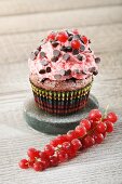 A chocolate cupcake decorated with strawberry cream, chocolate pearls and redcurrants