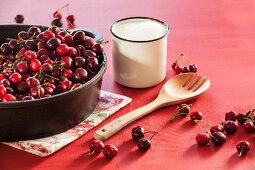 Cherries in a deep cast iron pan with a cup of sugar and a wooden spoon