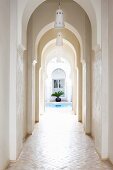 Narrow arcade in entrance area of Moroccan house with view of pool and palm trees in courtyard
