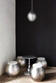 Barrel-shaped, metal stools, side table & pendant lamp in corner against black wall
