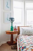 Bedroom with bed, patchwork bedspread & bedside table with round wooden top in bay window