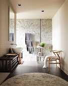 Modern bathroom with round rug on black tiled floor, floating washstand against wall & classic, wooden chair