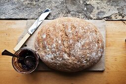 A whole loaf of homemade wholemeal bread and jam on a wooden board