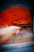 A pizza being pushed in to a hot, glowing wood-fired oven