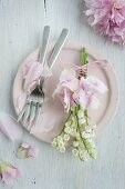 Posy of lily-of-the-valley and hydrangeas on pink plate scattered with peony petals