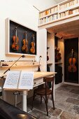 Living area in instrument-maker's workshop with vintage table, violins in display case, music stand and bookcase balustrade