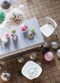 Romantisch dekorierter Esstisch mit verschiedenen Blumenvasen unter Glashauben, Luftballons am Fliesenboden und hängenden Pompons im Industrie-Ambiente