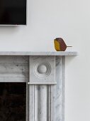 Small, minimalist wooden bird sitting on marble fire surround