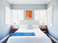 Schlichtes Doppelbett vor Fenster mit Ornamenten in schmalem Schlafzimmer, hellgraue Wände und gemaltes Frauenportrait im Retrostil