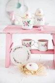 Tassen mit Blumenmotiven und Osterdeko auf rosa Schemel
