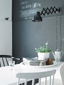 Weisser Esstisch vor schwarzer Wand mit schwarzer Wandleuchte im Retro Stil