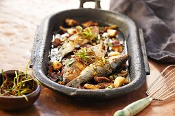 Roasted sardines with vegetables and herbs in an iron pan