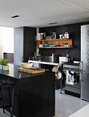 Black island unit opposite workbench-style kitchen counter and wooden shelves on dark wall