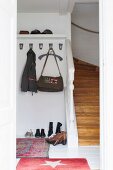 Garderobenhaken, Hutbord und Schuhe am Boden neben einem Treppenaufgang in weisser Diele mit roten Teppichen