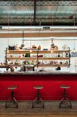 Bar in ehemaliger Werkstatt mit roter Bartheke, Vintage-Drehstühlen und langem Flaschenregal