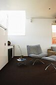 Sessel mit passendem Schemel auf dunklem Teppichboden in minimalistischem Zimmer