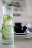 Glass carafe of water with lime peel in front of place setting with black bowl