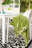 Hellgrünes Tuch auf weißem Stuhl vor Tisch, auf Boden schwarz-weiss gemusterter Teppich