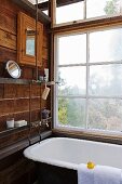 Old bathtub with exposed plumbing below lattice window