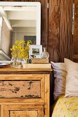 Flowers and mirrors on top of old cabinet next to bed