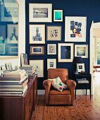 Brown leather armchair in corner of library with collection of pictures on blue-painted wall
