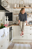 Frau in weisser Landhausküche übereck, an Holzwand Konsolenregal mit Geschirr