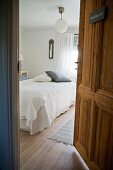 View of bed with white bedspread and scatter cushions in rustic bedroom seen through open door