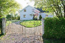 Schmiedeeisernes Tor vor Garten und Landhaus mit hellgrauer Holzverschalung