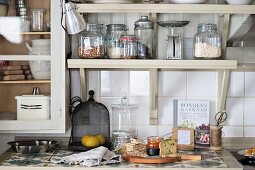 Food preparation on kitchen worksurface below storage jars on bracket shelves
