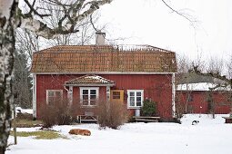 Blick über verschneiten Garten auf rotbraunes Holzhaus mit weissen Fenstern