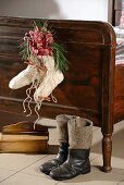 Wollsocken mit Orchideenblüten und Zimtstangen als Weihnachtsdekoration an Holzbettgestell, davor Vintage Stiefel