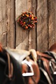 Blick über Pferdesattel auf Blumenkranz an Bretterwand aufgehängt