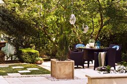Gartenmöblierung und Pflanzenbehälter mit Zypresse auf gepflasterter Fläche in sonnigem Garten einer alten Villa