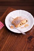 A slice of apple strudel with icing sugar and cream