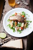Grilled Cajun salmon steak on a bed of potato wedges and rocket and tomato salad with Parmesan