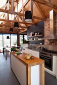 Schmale Holztheke mit Schrankunterbau in offener hoher Designerküche; sichtbare Dachkonstruktion mit montierten schwarzen Pendelleuchten