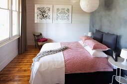 Double bed with red and white striped bed linen against grey wall and white wooden wall in background in rustic, modern bedroom