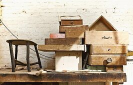 Various old wooden drawers stacked on workbench against whitewashed brick wall