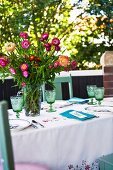 Summer bouquet in glass vase on garden table set for meal