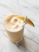 A melon and peach smoothie made with soy milk in a glass garnished with a melon wedge